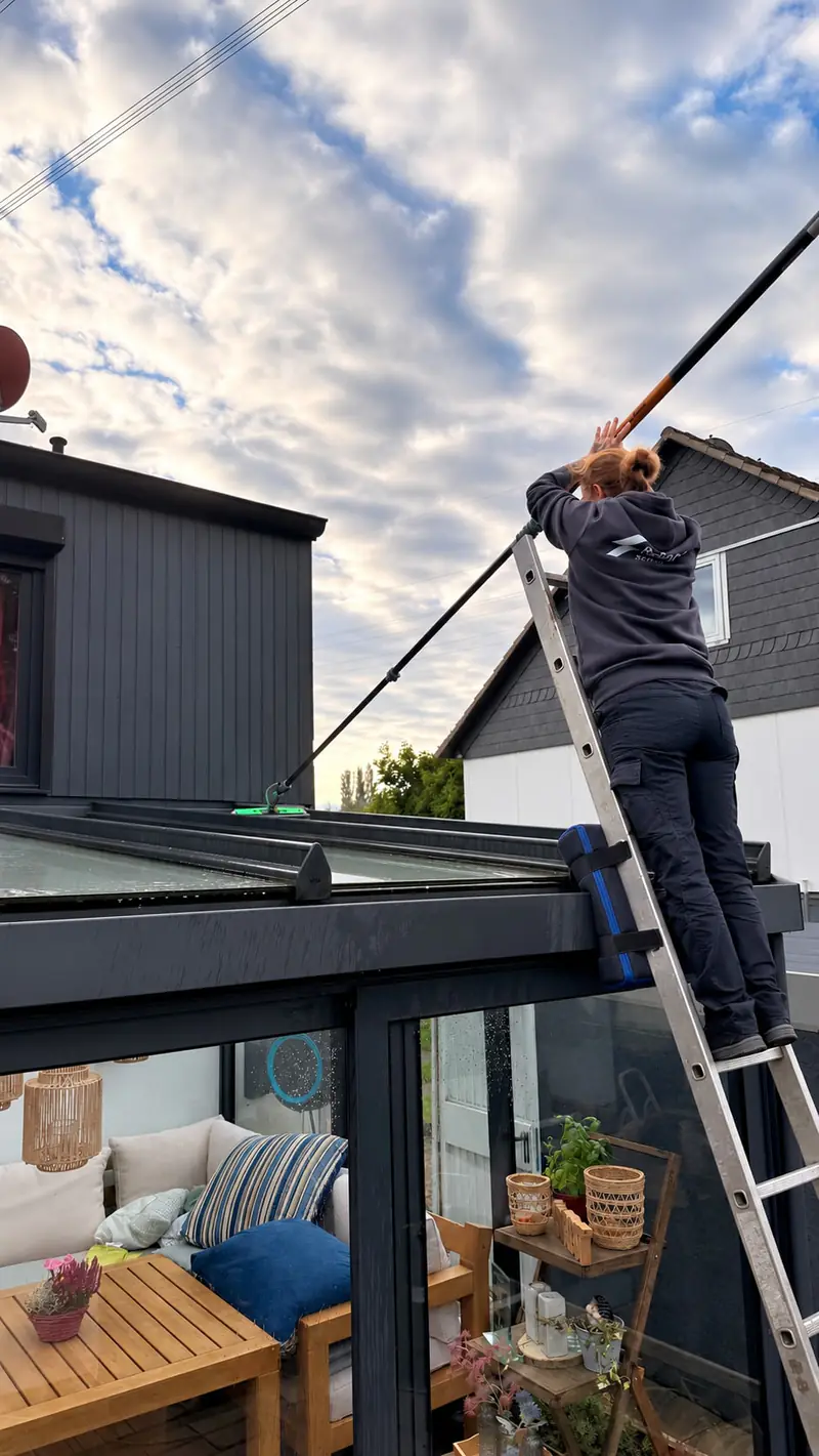 Mitarbeiterin von Reingart Service reinigt das Glasdach eines Wintergartens mit einer Teleskopstange