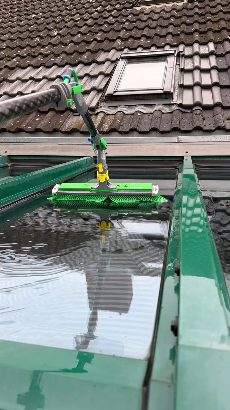 Glasdach eines Wintergartens wird mit Wasserbürste und Teleskopstange gereinigt