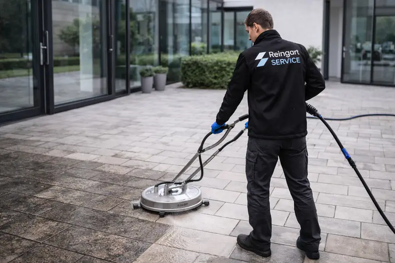 Mitarbeiter von Reingart Service reinigt eine gepflasterte Terrasse mit einem Flächenreiniger