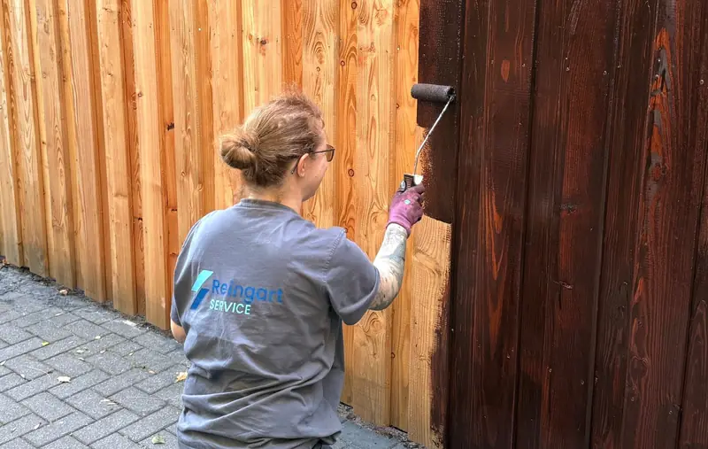 Mitarbeiterin von Reingart Service streicht einen Holzzaun